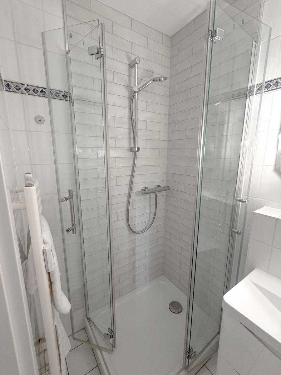 Shower cabin with glass door, showerhead, and handheld shower, white tiles, and towel rack.