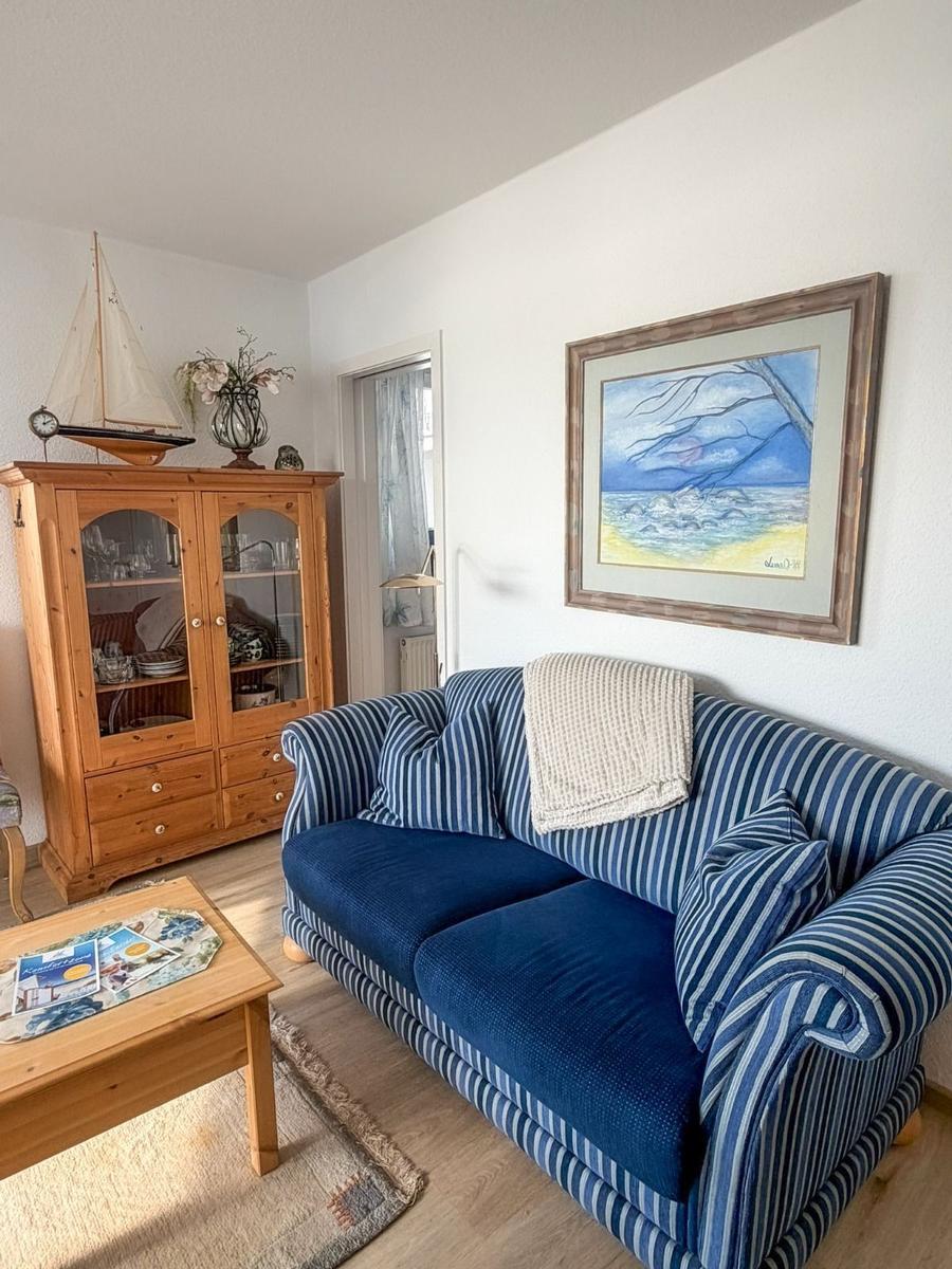 Living room with sofa, wooden cabinet, and wall painting. Wooden floor and rug.