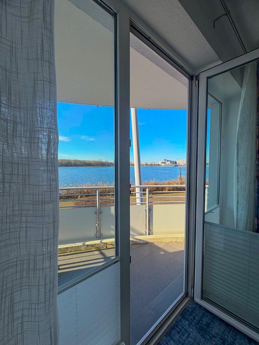 View of a lake from the balcony with glass door and white railings.