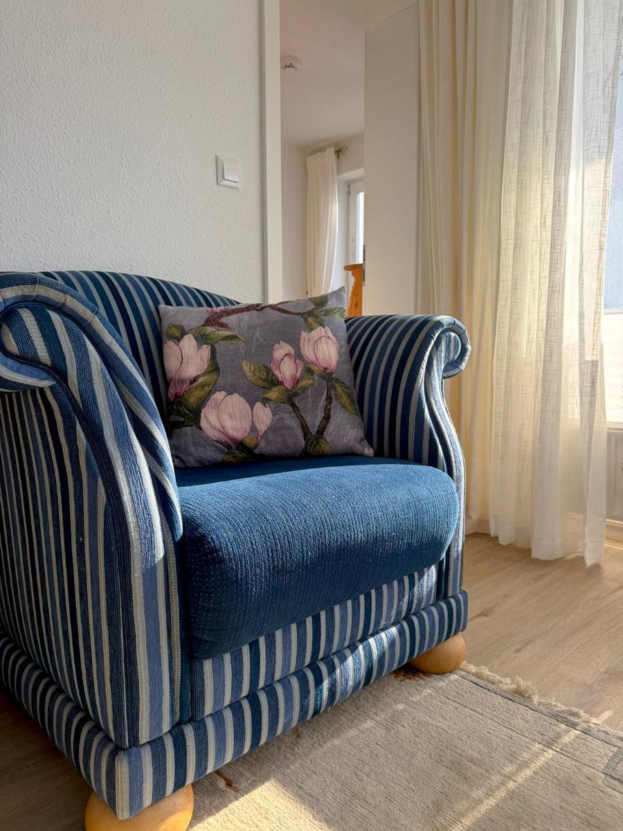 A blue striped armchair with a floral cushion stands near a window with curtains.