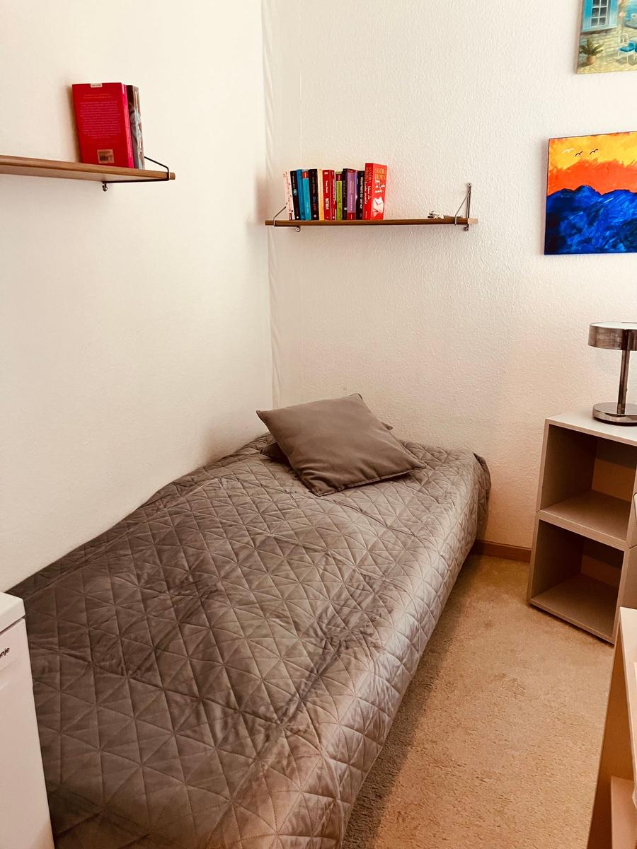 A bedroom with a single bed, wall shelves, and a bedside lamp.