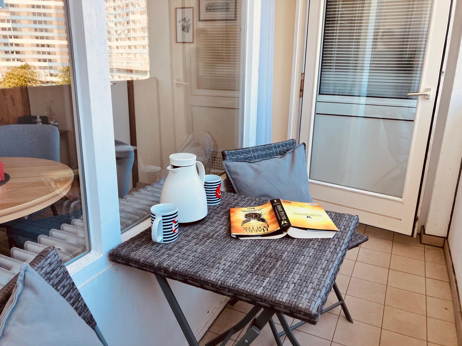 Balcony with table, chairs, and book. View of high-rise buildings.