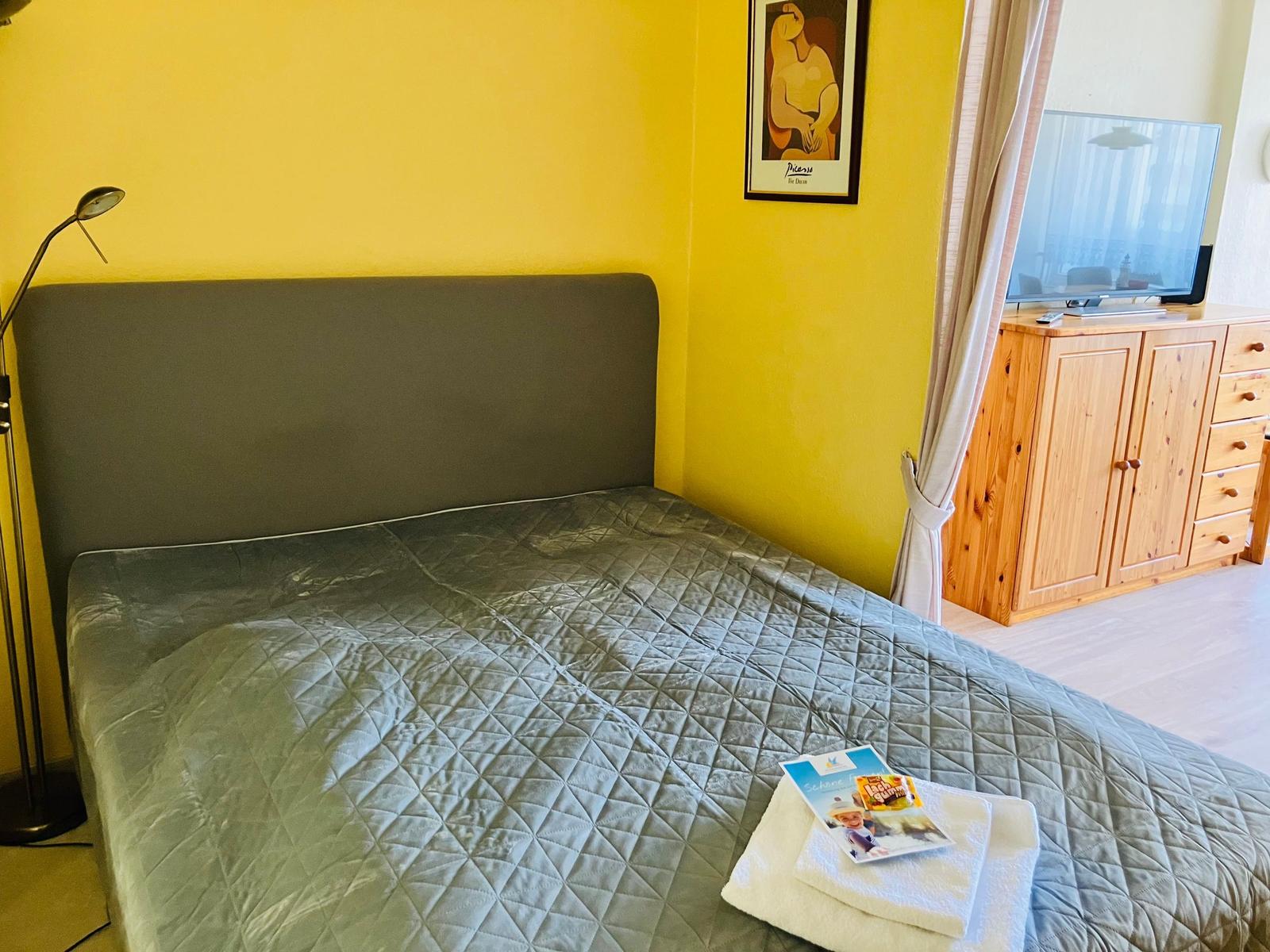 Bedroom with bed, TV, and wooden cabinet. Yellow walls and comfortable furnishings.
