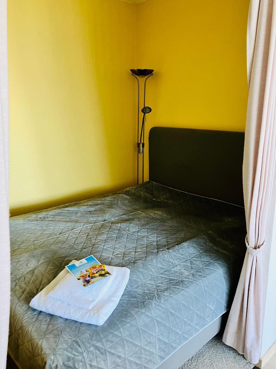 Bedroom with yellow walls, bed with gray quilted cover, and floor lamp.