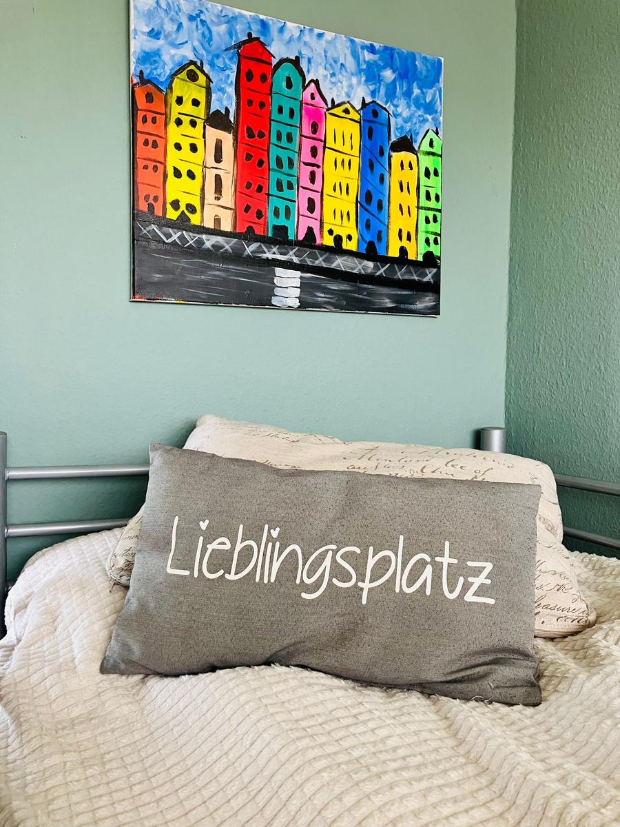 Bettkopf mit Kissen und Wandbild von bunten Häusern.