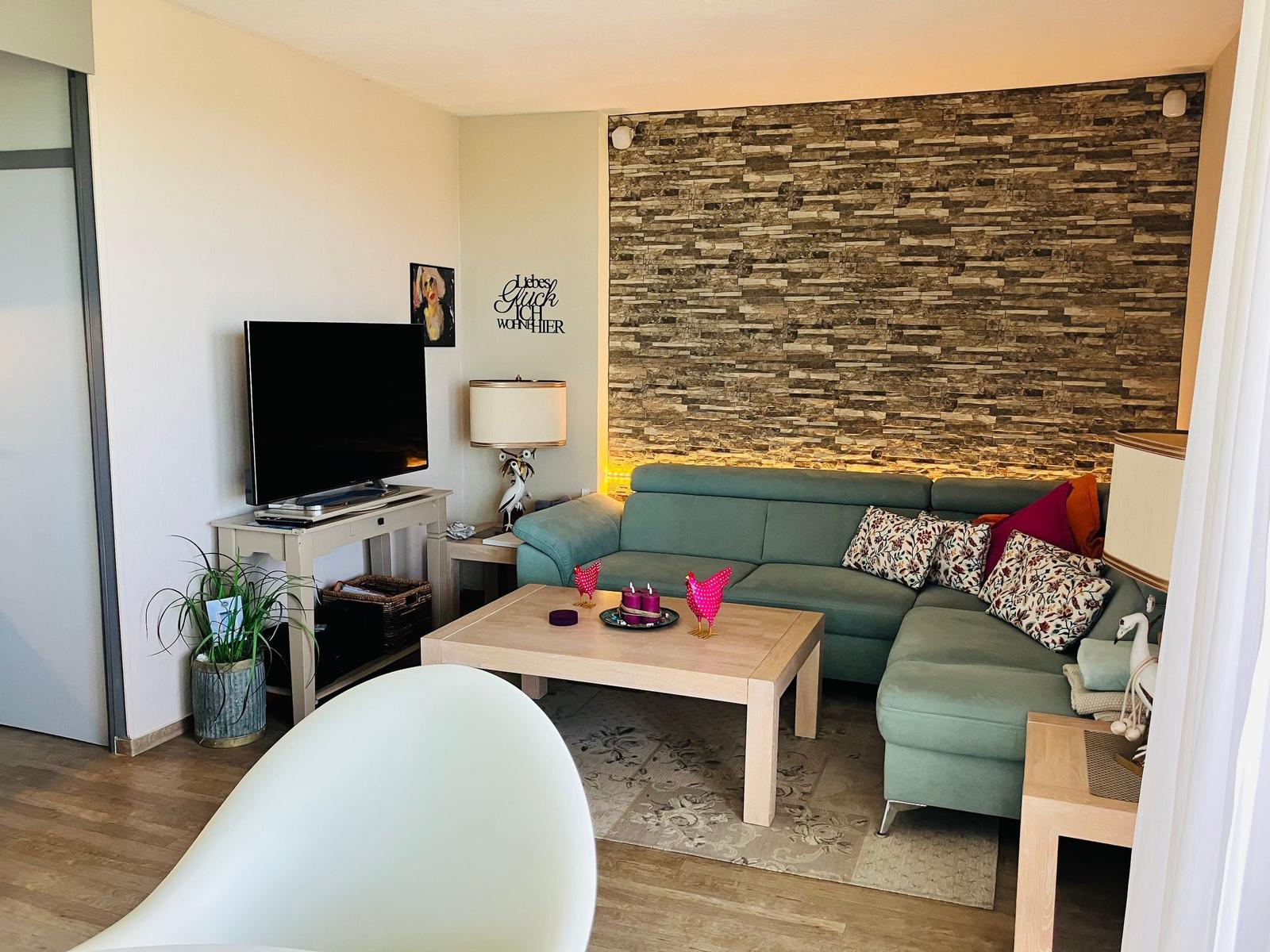 Ein Wohnzimmer mit grünem Sofa, Holztisch und Steinwand im Hintergrund.