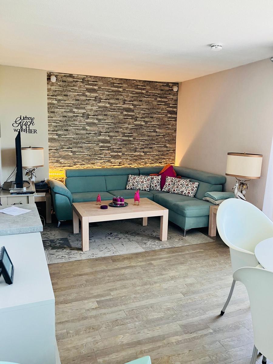 Wohnzimmer mit Sofa, Couchtisch und Holzboden. Hintergrundwand aus Steinoptik.