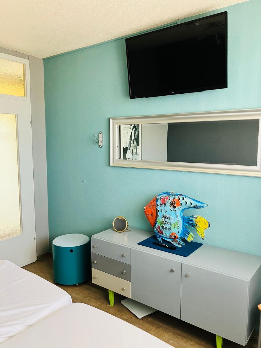 Zimmer mit TV, Spiegel und buntem Fischobjekt auf Schrank.