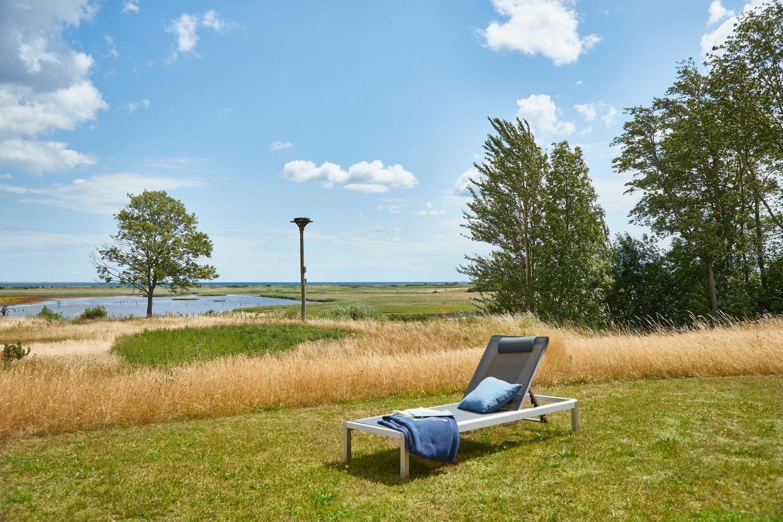 Liegestuhl auf grünem Rasen mit Blick auf Fluss und Himmel.