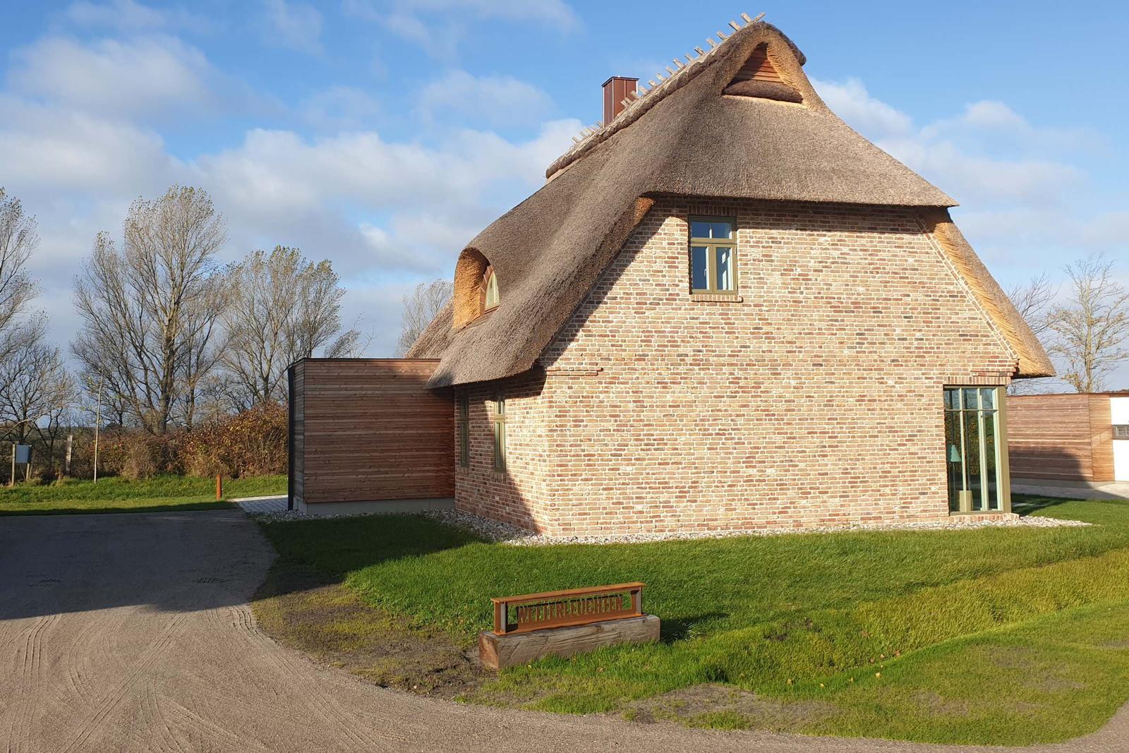 Haus mit strohgedecktem Dach und Backsteinfassade auf grünem Grundstück.