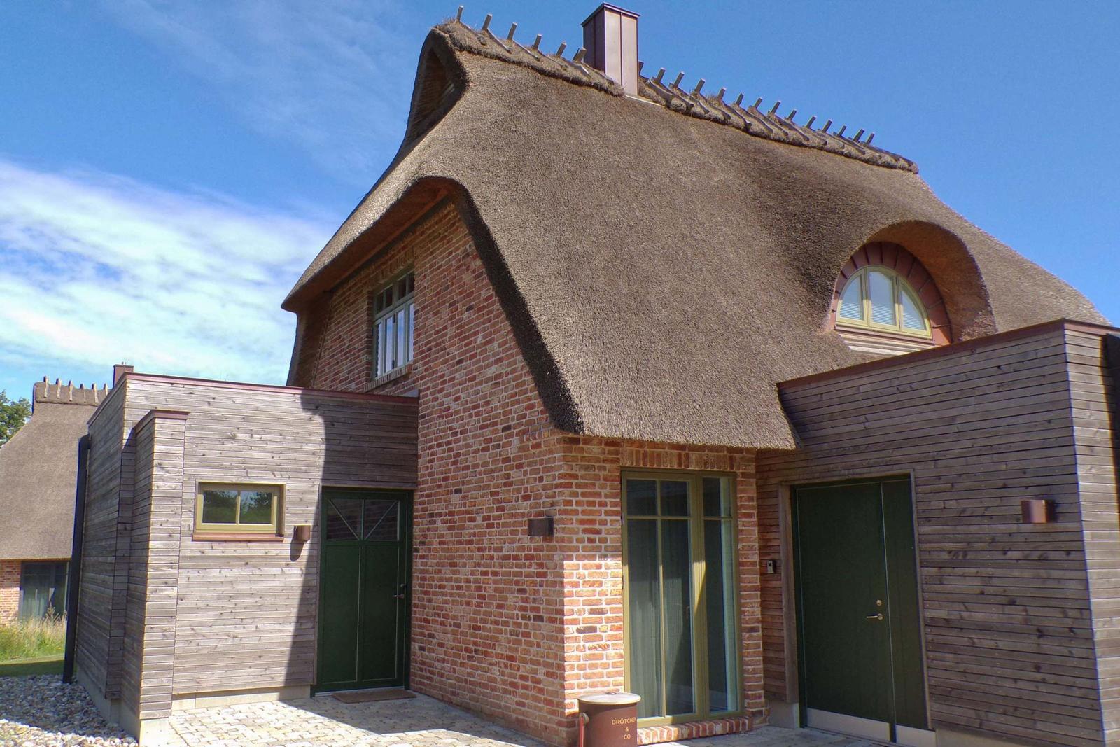 Haus mit strohgedecktem Dach und Backsteinfassade. Holzverkleidung an Nebengebäuden. Grünfarbene Türen.