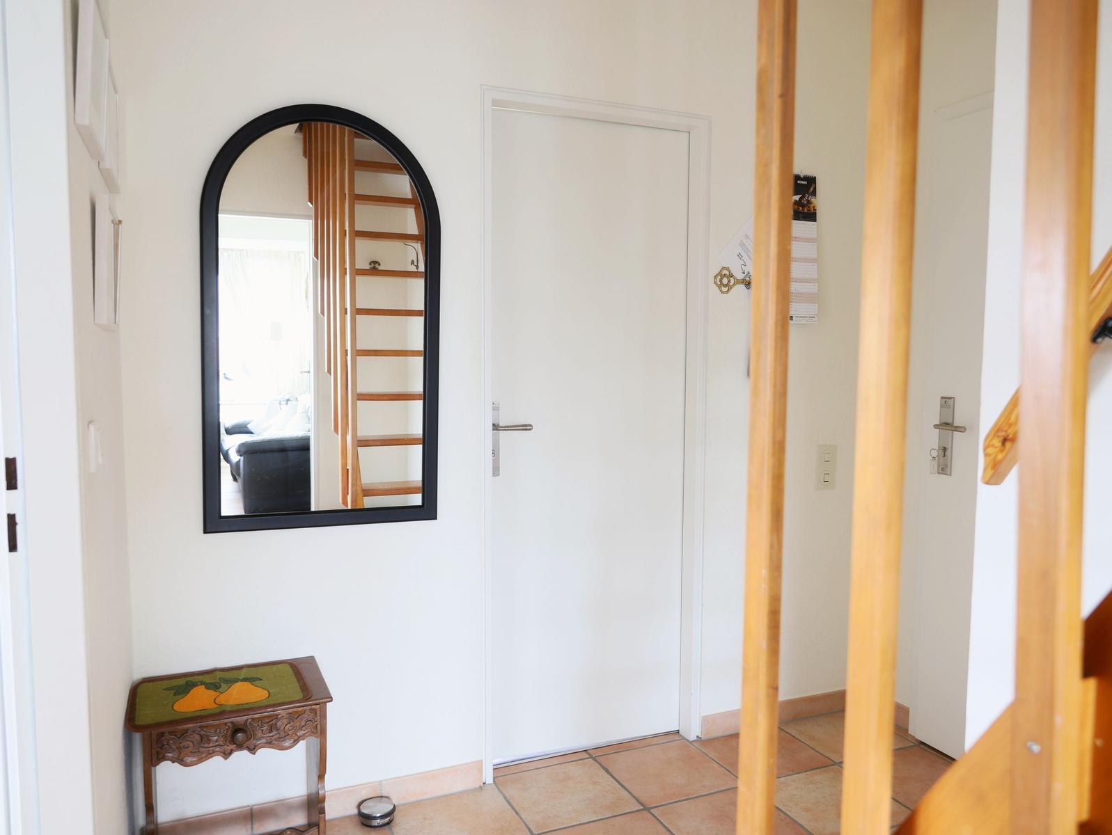Eingangsbereich mit Spiegel, Tür und Holztreppe.