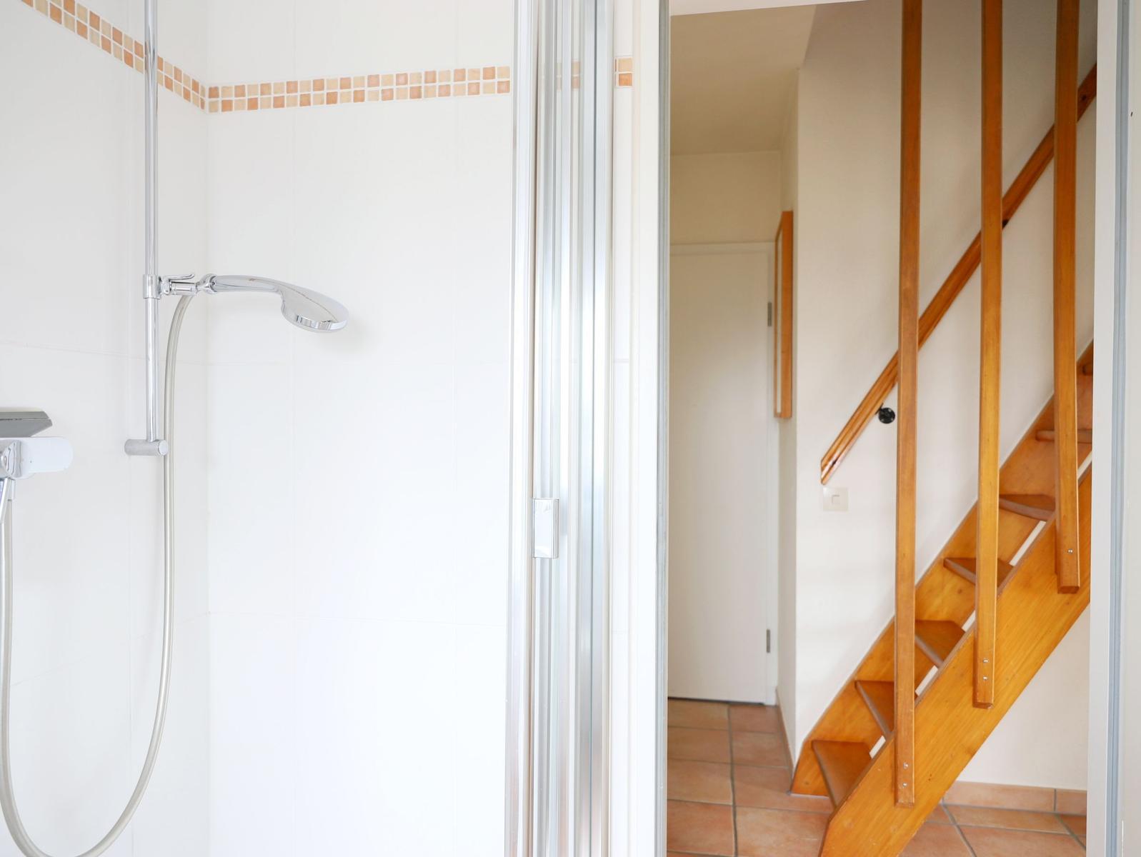 Dusche mit Glaswand und Holztreppe im Hintergrund.