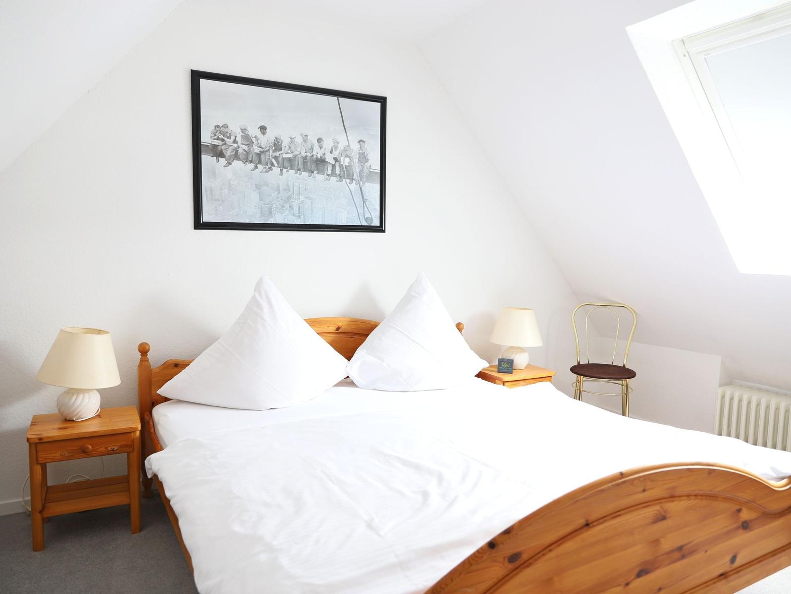 Doppelbett mit weißen Bettwäsche, zwei Nachttische und Stuhl unter Dachschräge.