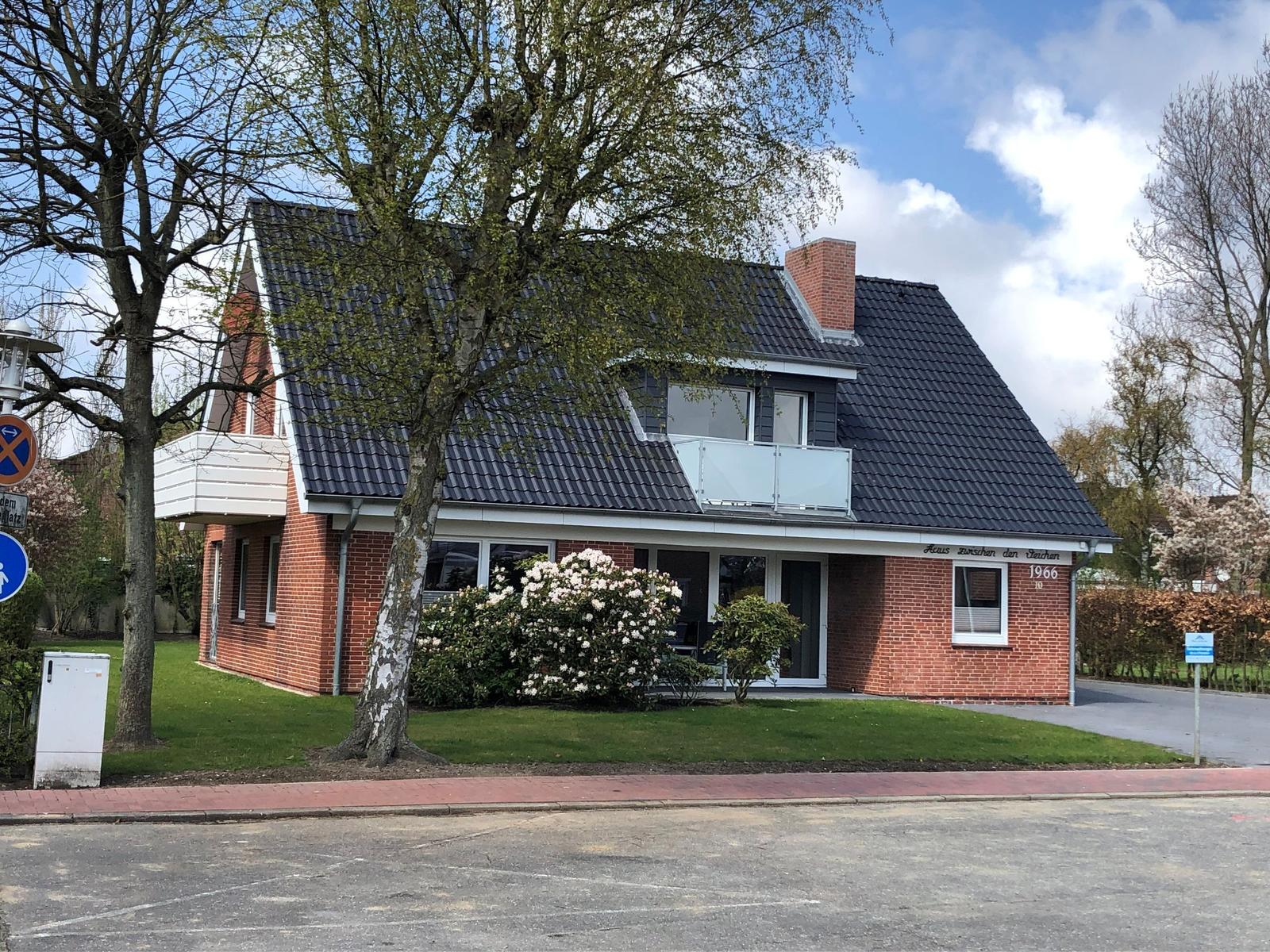 Ein zweistöckiges Haus mit rotem Ziegel und dunklem Dach, umgeben von Grünflächen und Bäumen.