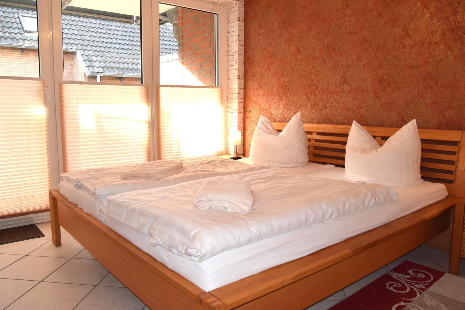 Ein Schlafzimmer mit einem Holzbett, weißen Bettwäsche und einem Fenster mit Jalousien.