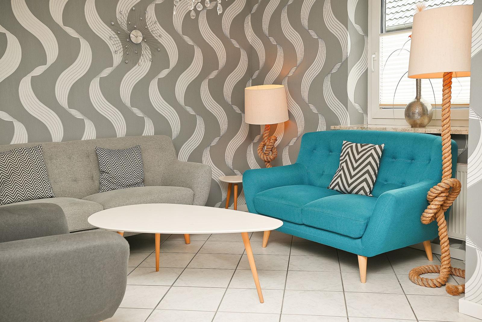 Ein Wohnzimmer mit grauem Sofa, türkisfarbenem Sessel und einem weißen Tisch.