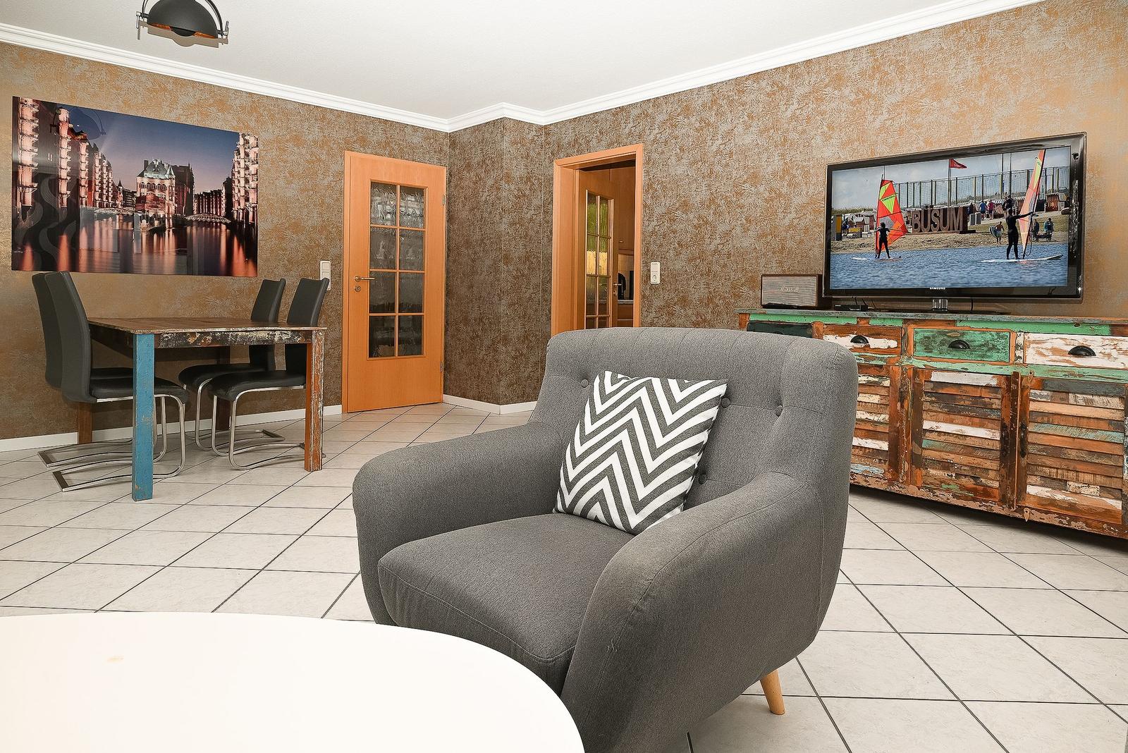 Wohn- und Essbereich mit Sofa, TV und Tisch. Wandbild und Holzfronten.