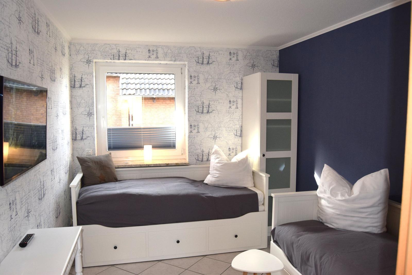 Schlafzimmer mit zwei Betten, Wand mit Seekartenmotiv und Fenster mit Jalousie.
