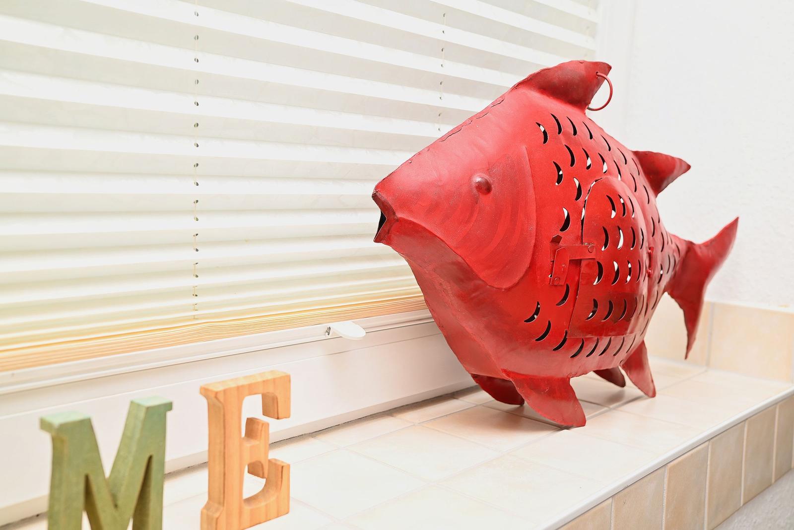 Roter Fischskulptur auf Fensterbank neben Buchstaben ME