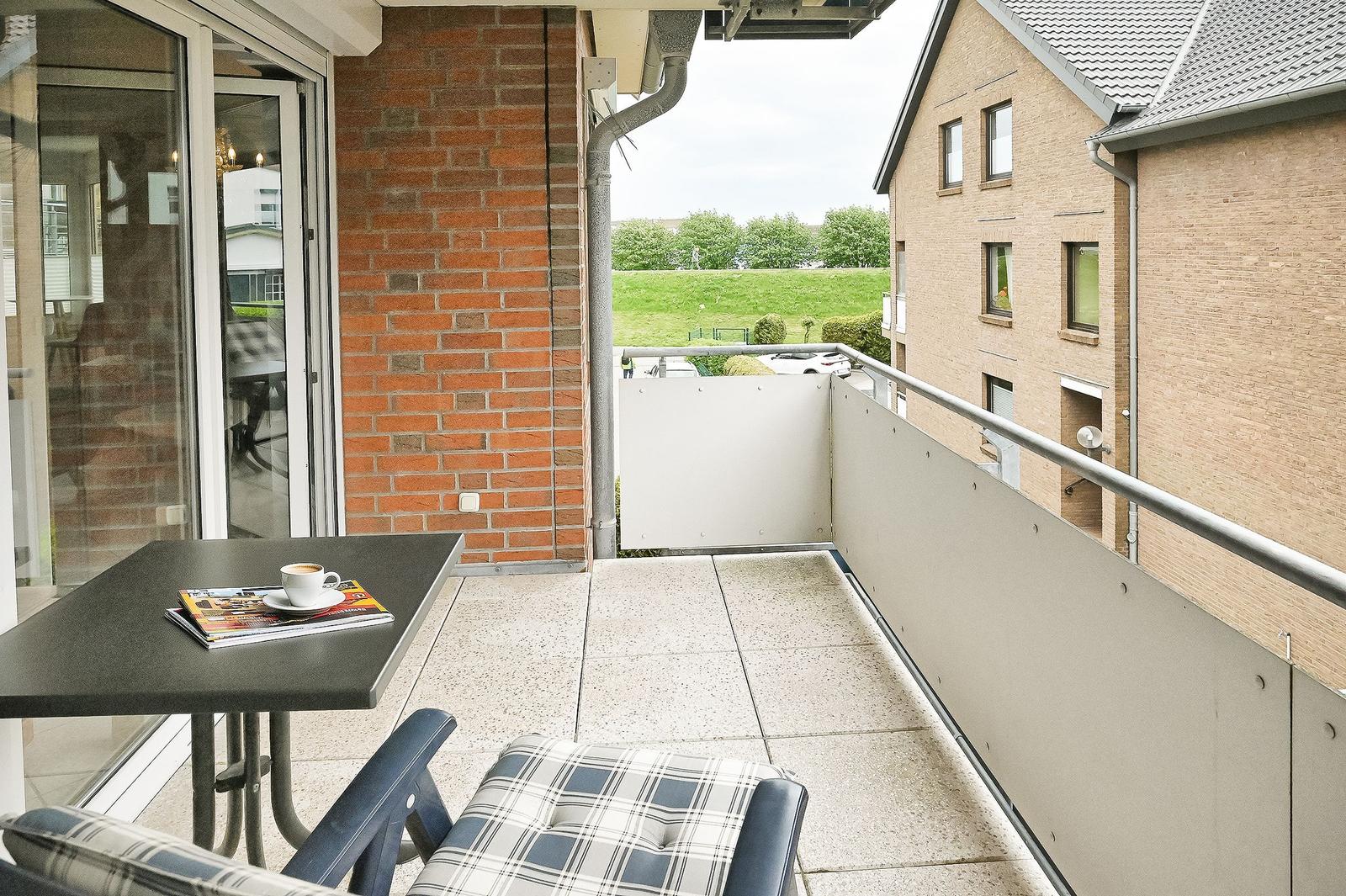 Balcony with table, chair, and cup. View of grass and building.
