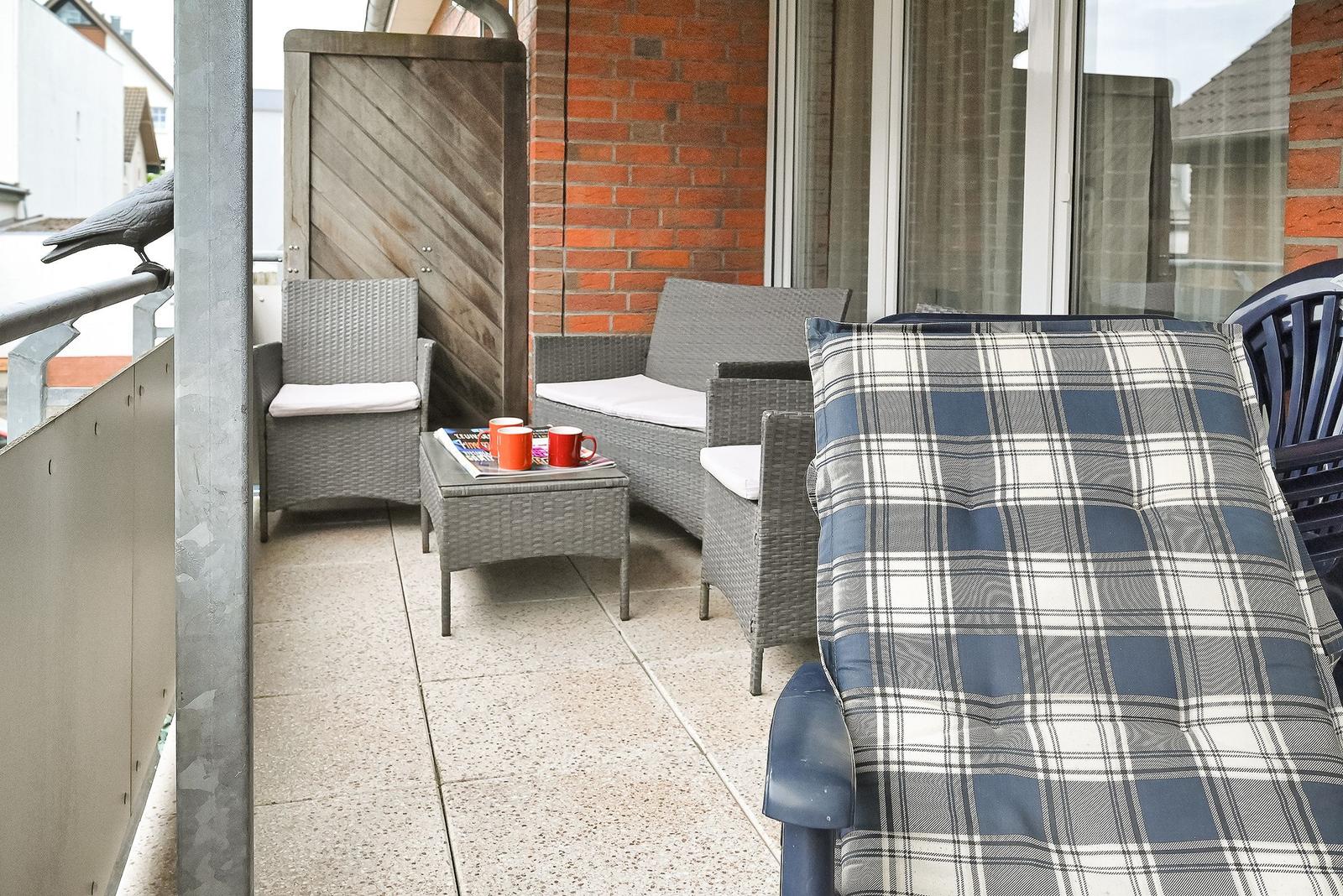 Terrasse mit Gartenmöbeln, Tisch und Kaffeetasse. Blick auf roten Backsteinbau.