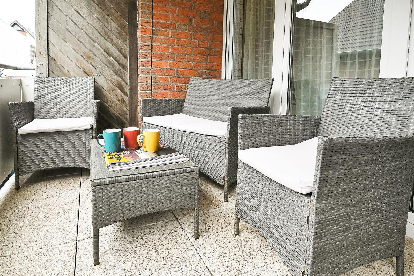 Terrasse mit grauen Rattanmöbeln, weißer Sitzauflage und Tisch mit Tassen.