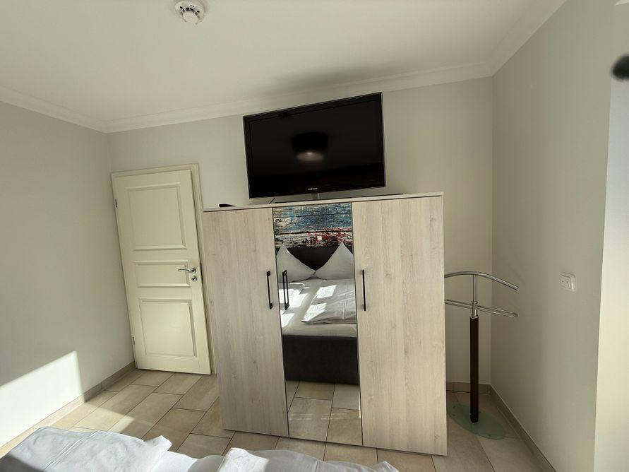 Bedroom with wardrobe, TV, and bed. Door and clothes stand are visible.