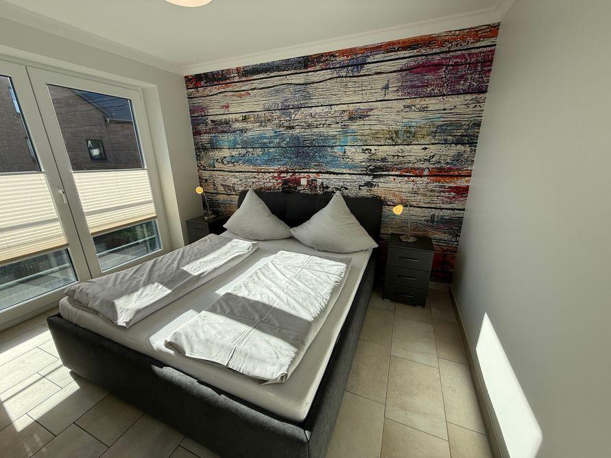Bedroom with double bed, colorful wall mural, and window to terrace.