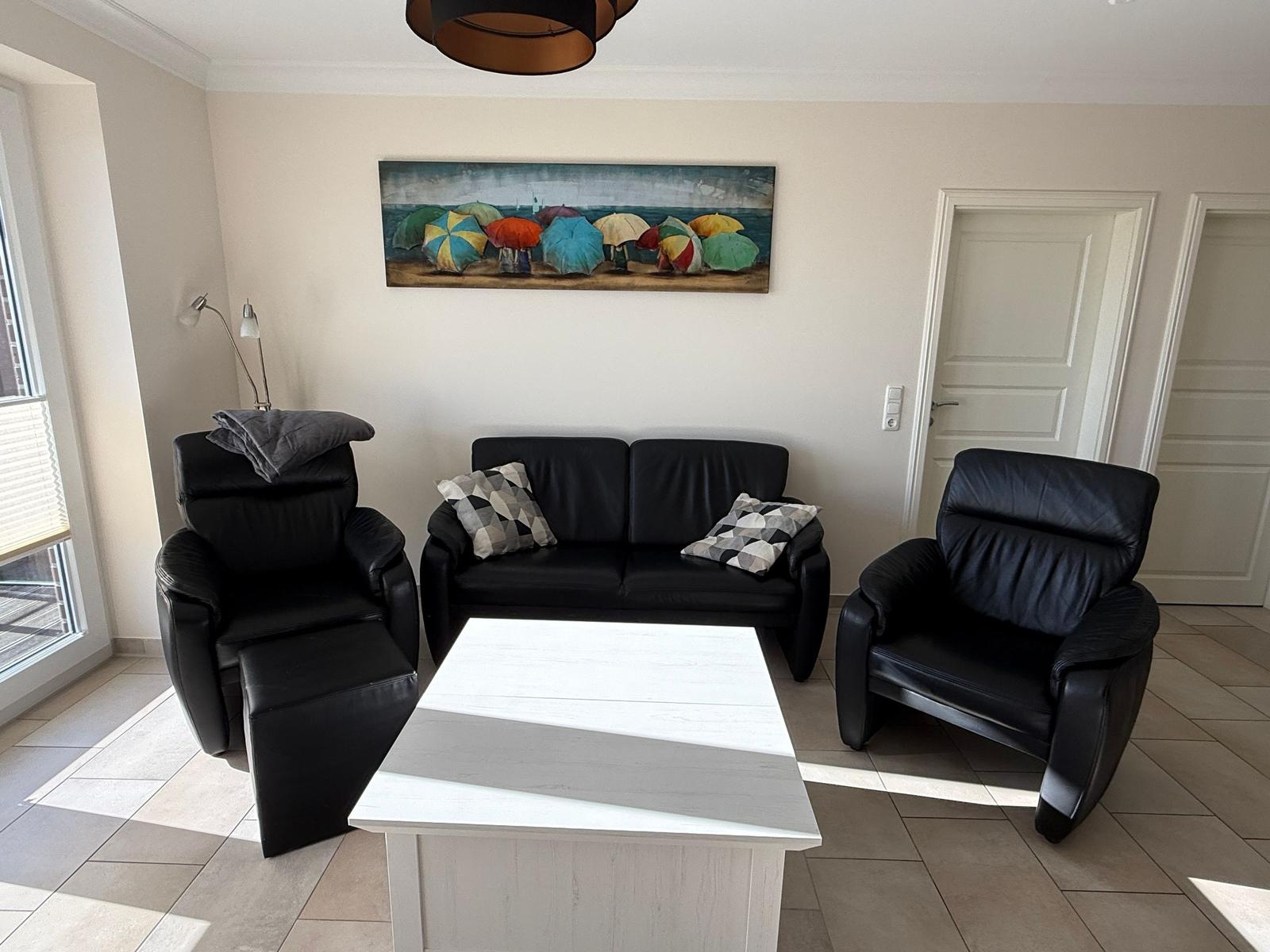 Living room with black sofa, two chairs, and white table. Wall art with colorful umbrellas.