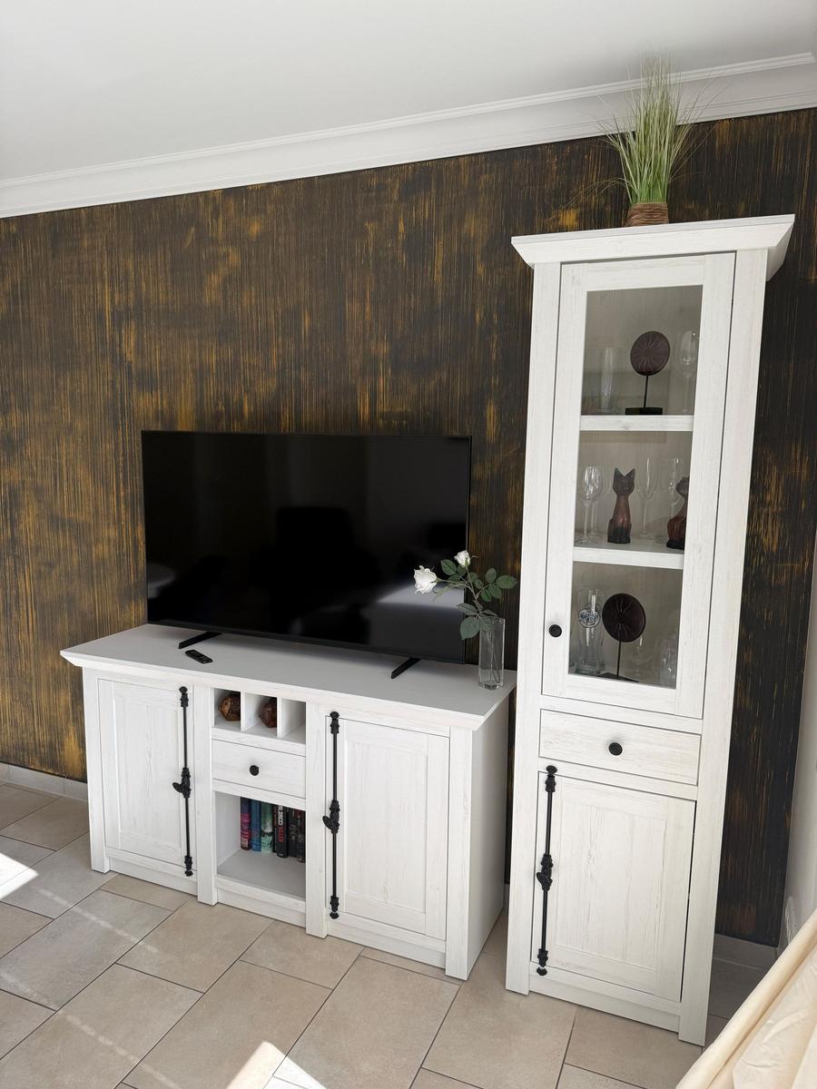TV stand and tall cabinet in white with glass doors and decor.