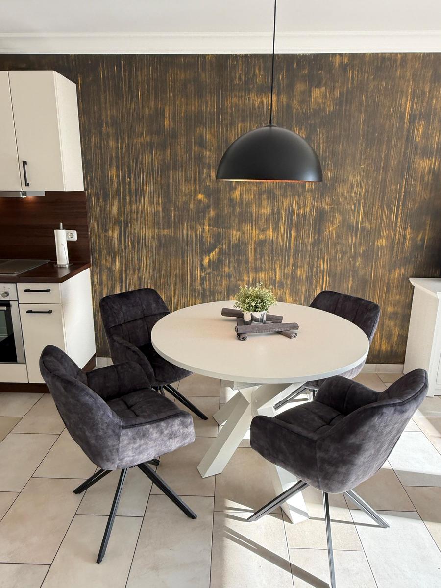 Round table with four chairs and pendant lamp against gold wall.