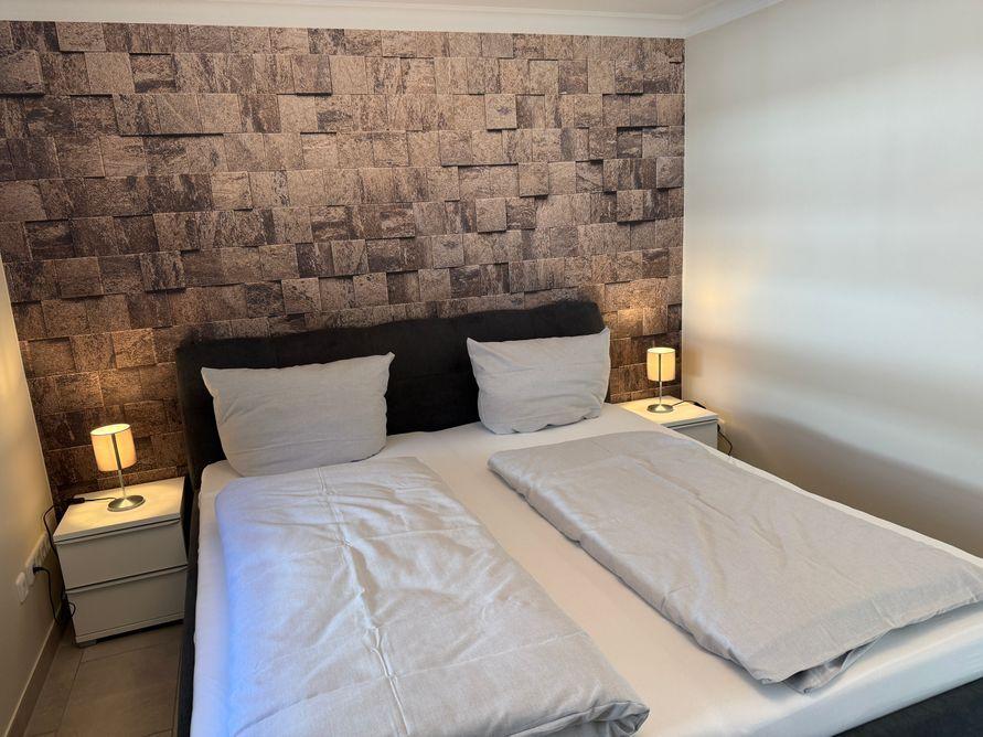 Bedroom with double bed, stone wall, and nightstands with lamps.