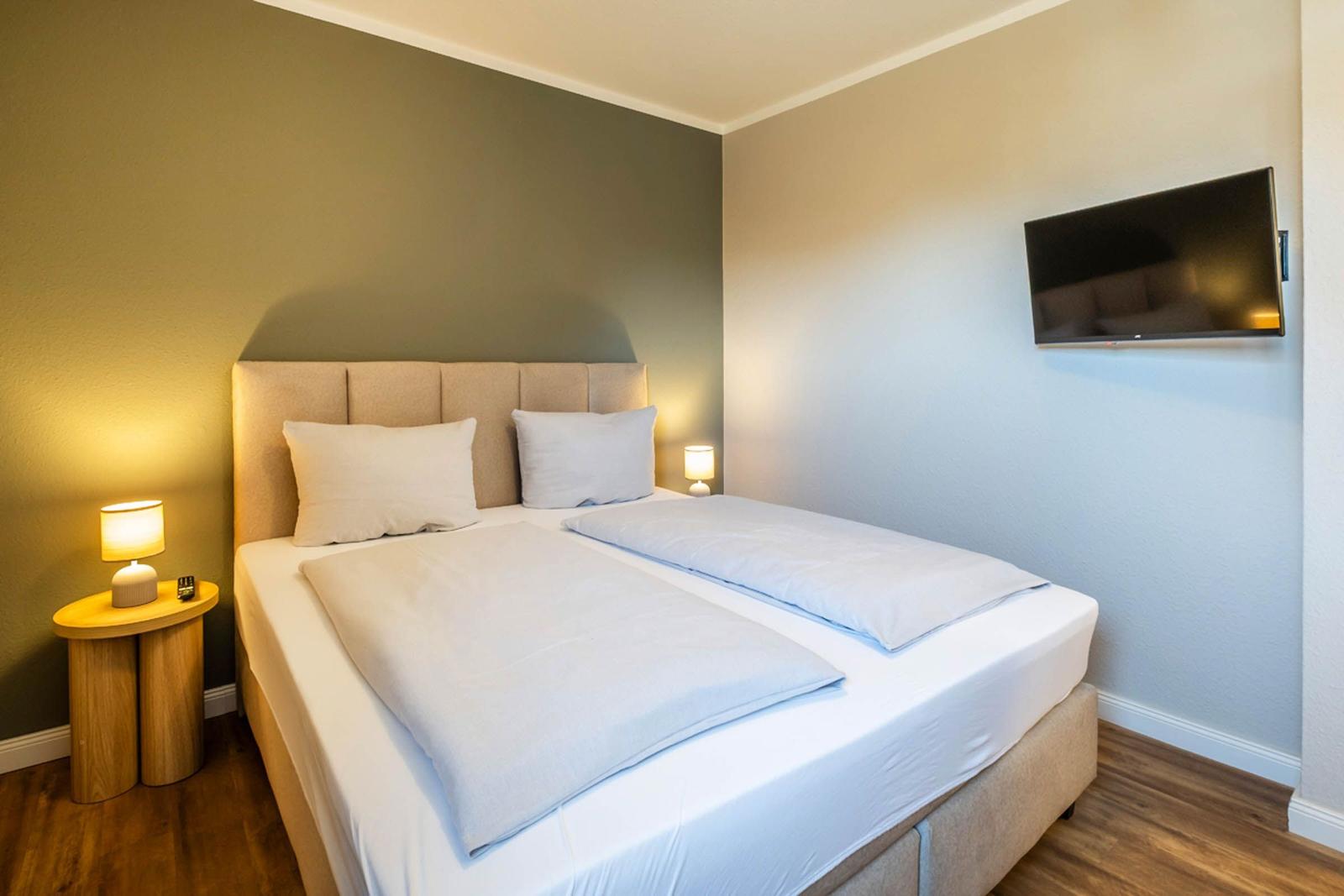 Ein Schlafzimmer mit Doppelbett, zwei Nachttischen und Fernseher an der Wand.