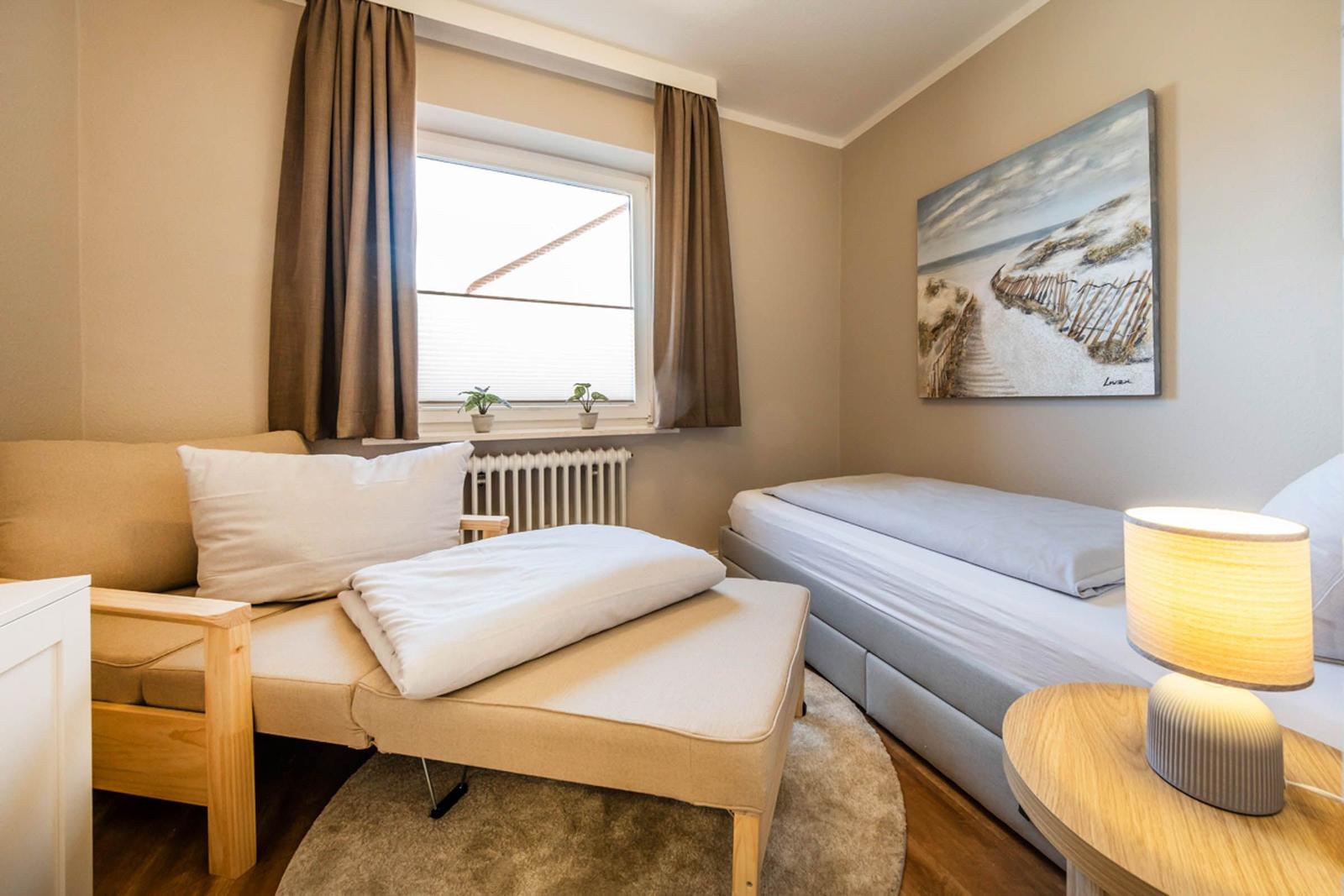 Ein Schlafzimmer mit Bett, Sofa und Fenster. Wandbild zeigt Strand.