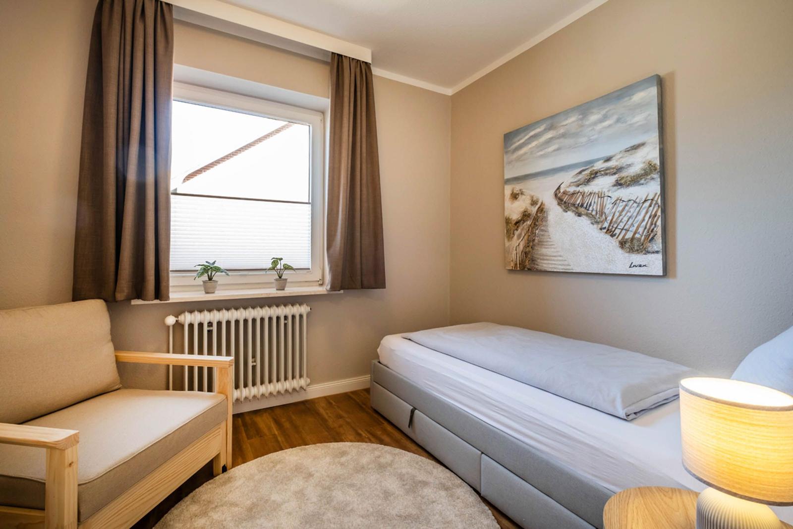 Schlafzimmer mit Bett, Sessel und Wandbild. Fenster mit Jalousie und Vorhängen.