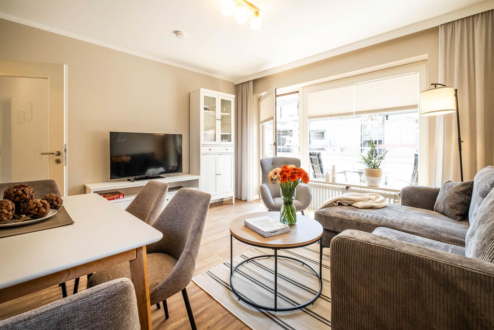Wohn- und Essbereich mit Sofa, Tisch, Fernseher und Fenster