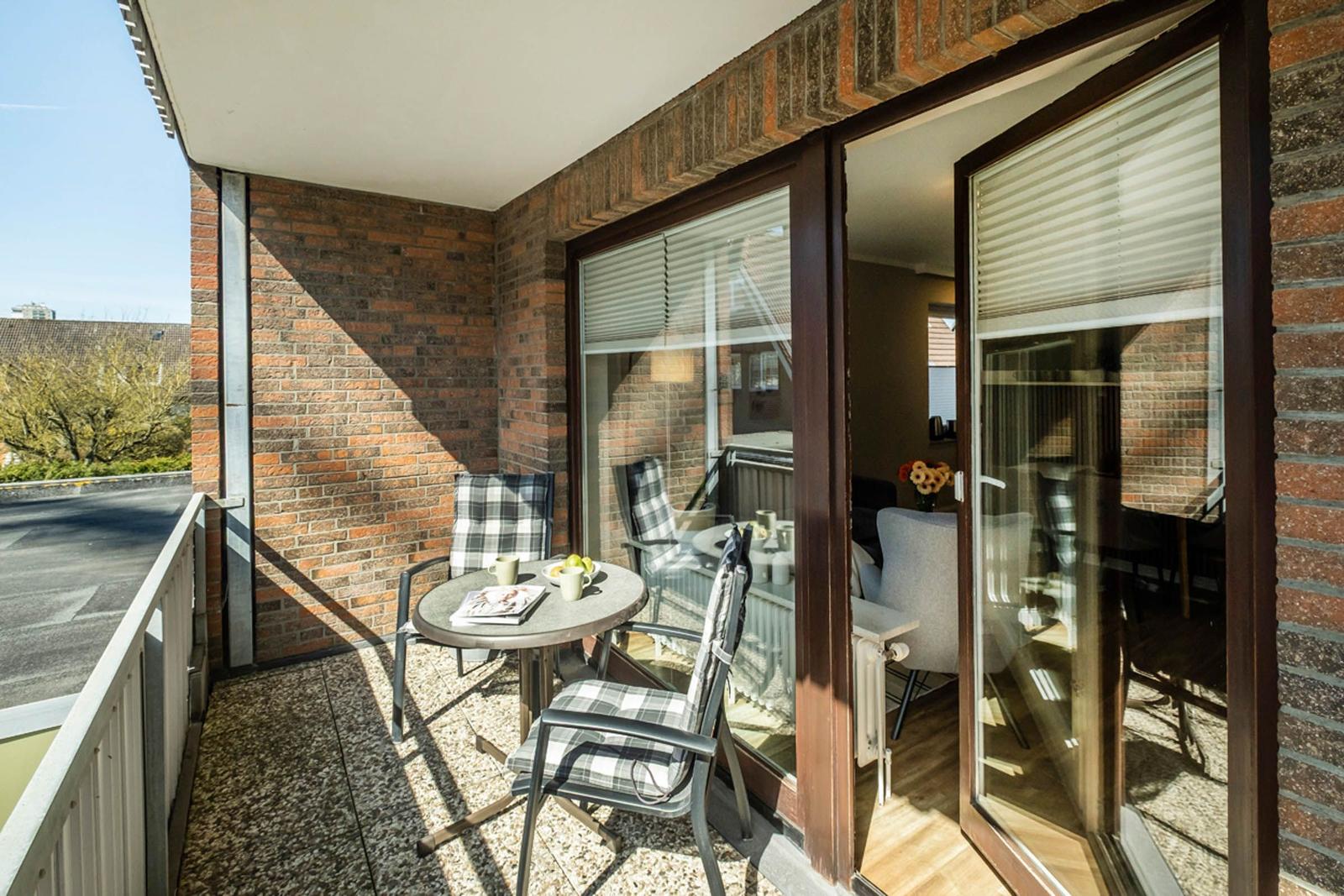 Terrasse mit Tisch und Stühlen, Sicht in Wohnzimmer mit Fenstern und Vorhängen.
