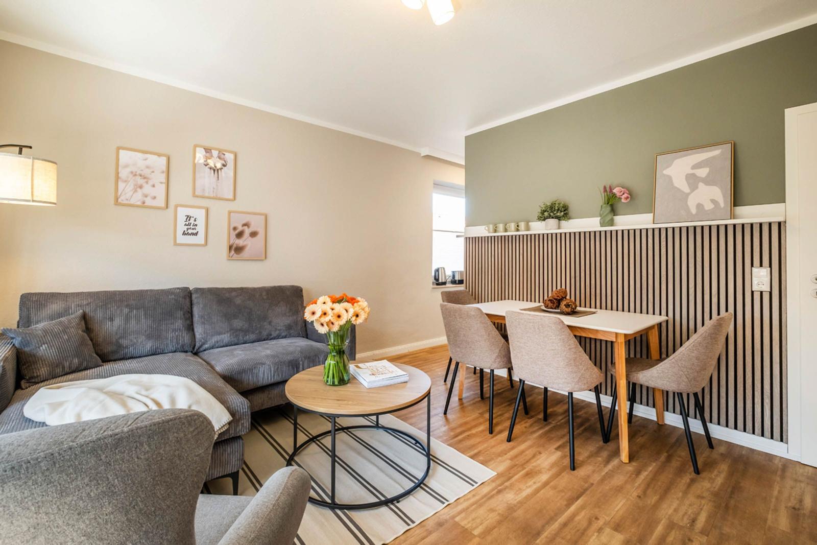 Wohn- und Essbereich mit Sofa, Tisch und Stühlen. Holzfußboden und Wandgestaltung.