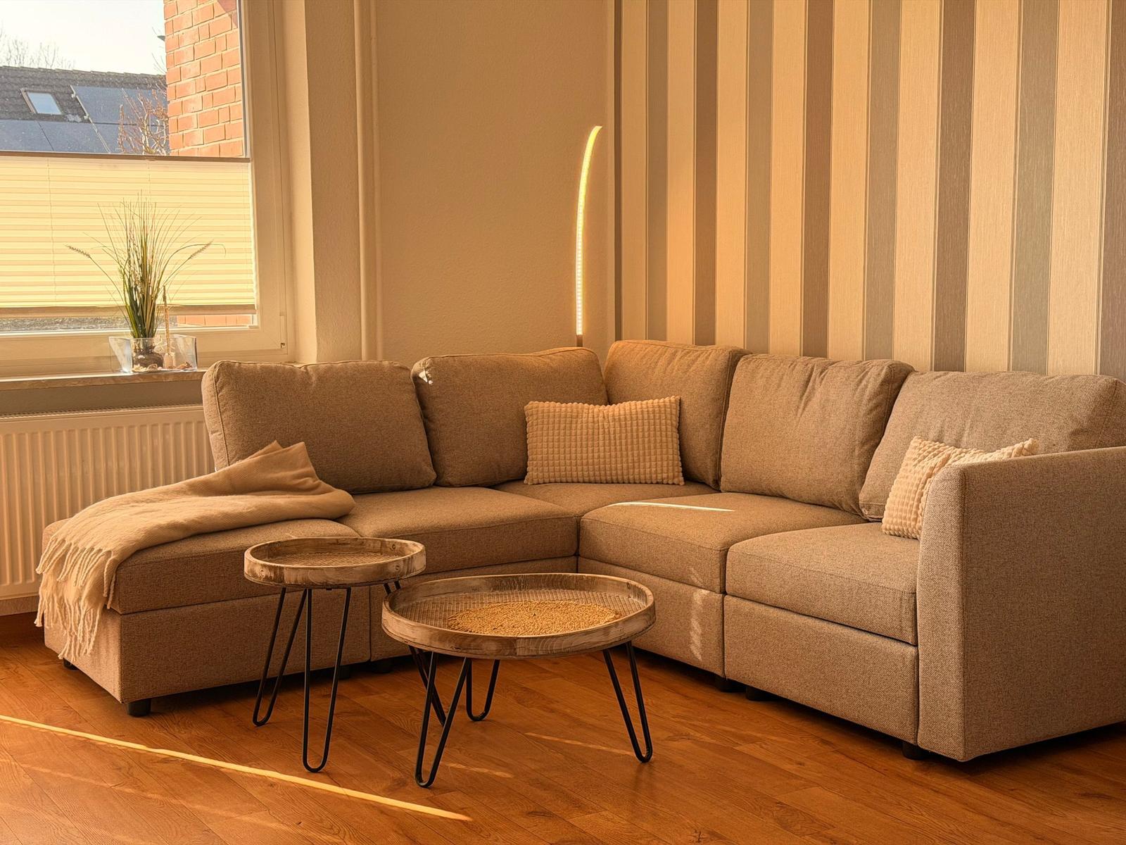 Ein Wohnzimmer mit Ecksofa, zwei runden Tischen und einer Streifenwand.