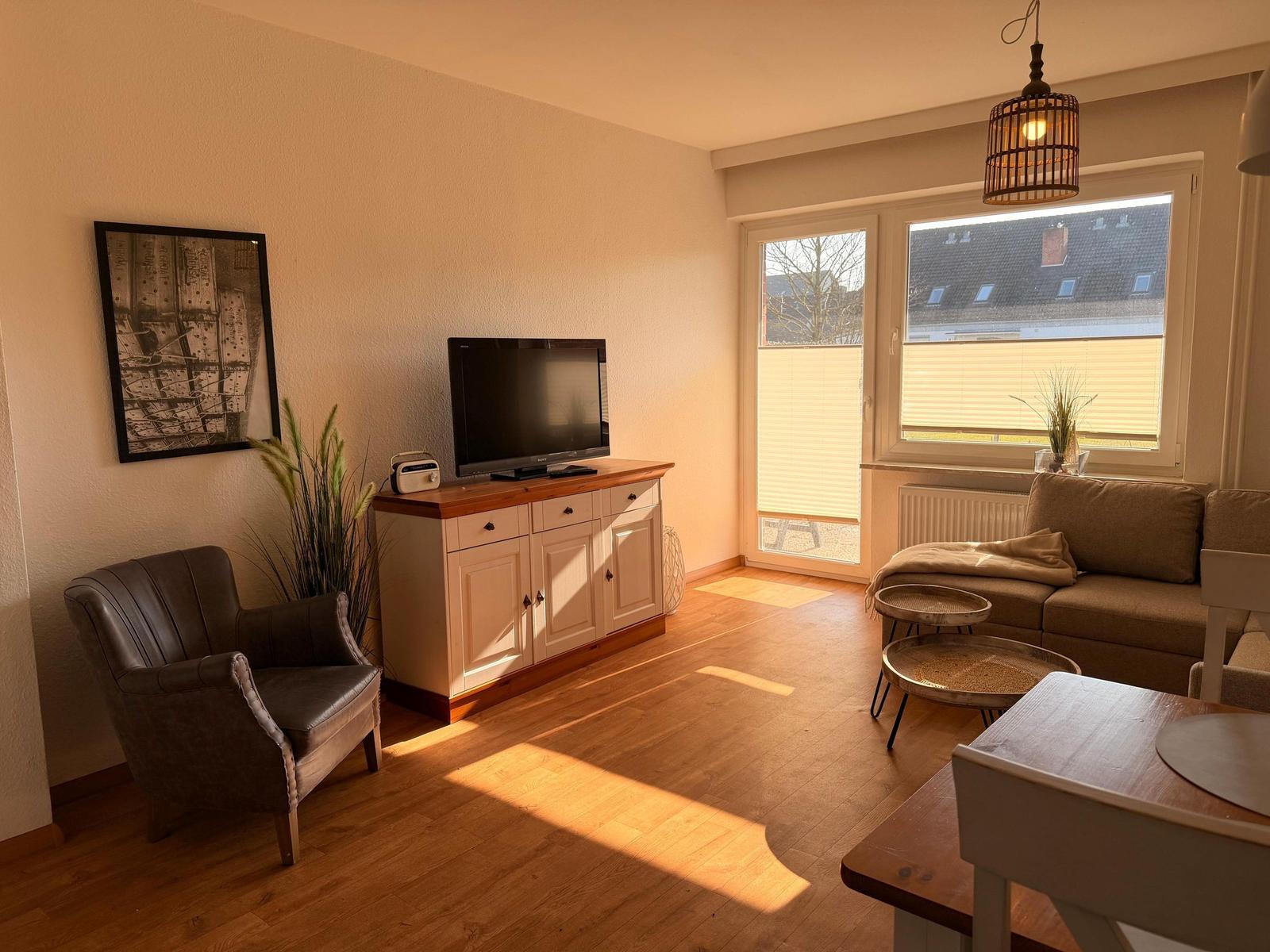 Wohnzimmer mit Sofa, Fernseher und Holzboden. Fenster mit Blick auf Dach