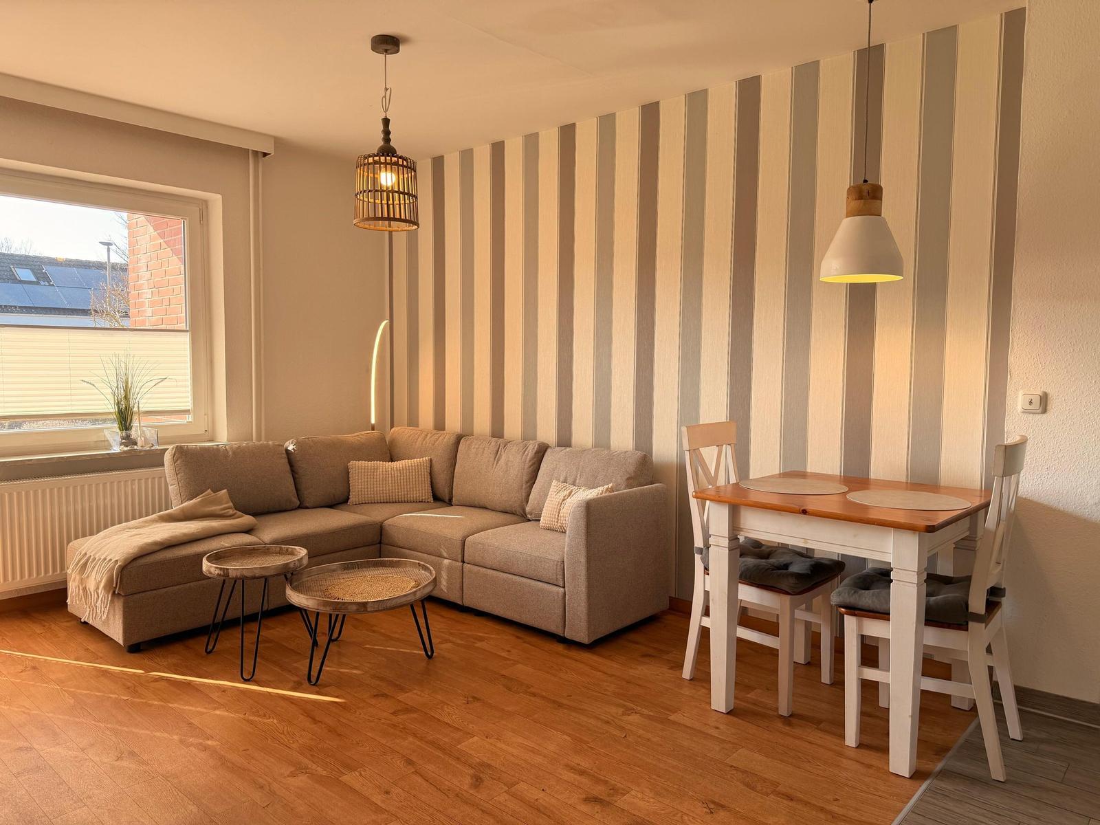 Wohn- und Essbereich mit Sofa, Tisch und Stühlen. Streifenwand und Holzboden.