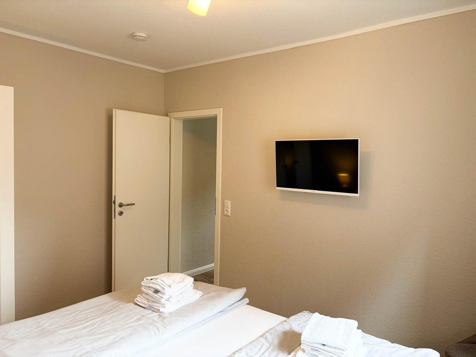 Bedroom with bed, towel stack, and wall-mounted TV. Door leads to adjacent room.