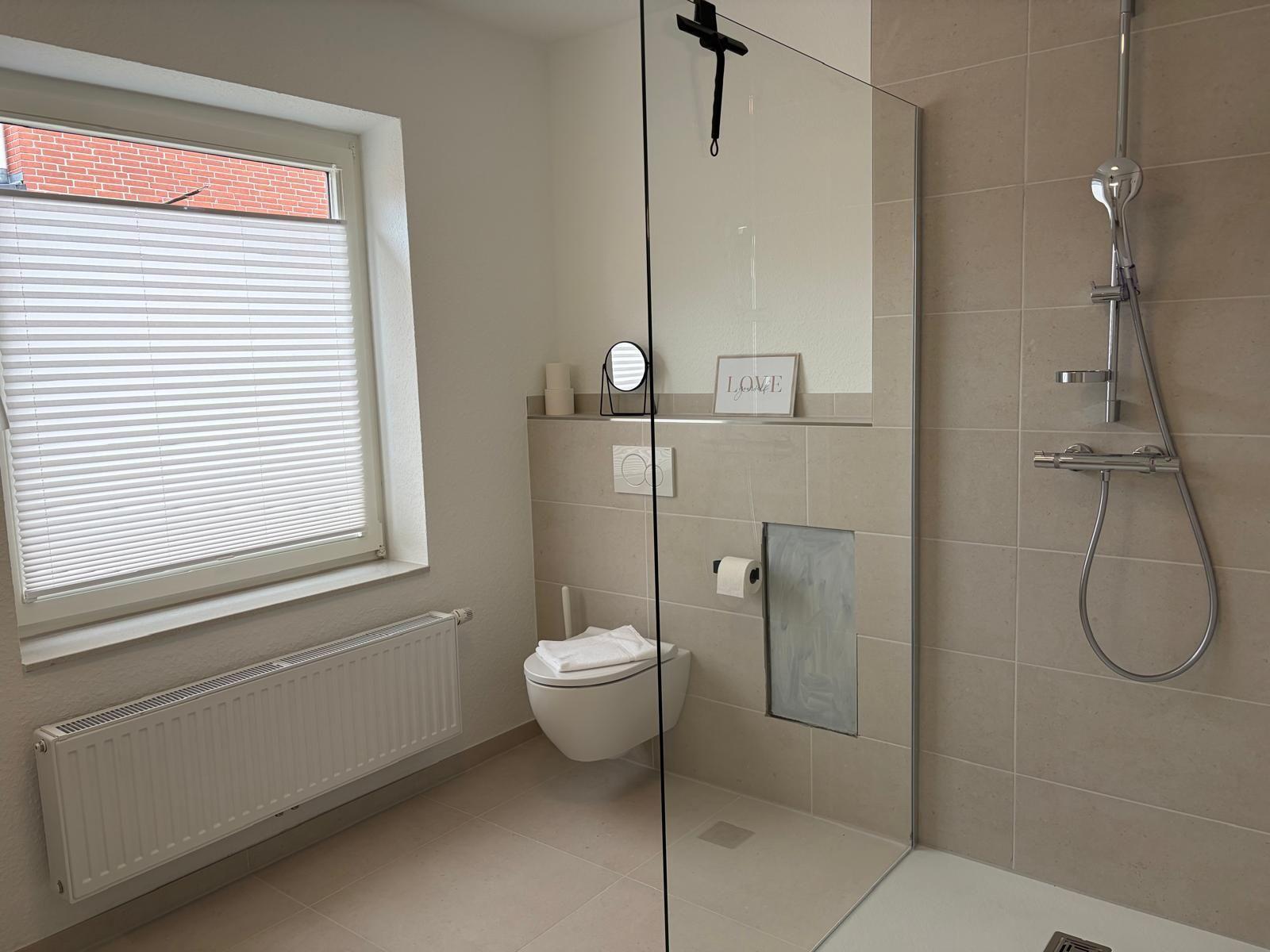 Bathroom with shower, toilet, and window with blinds.