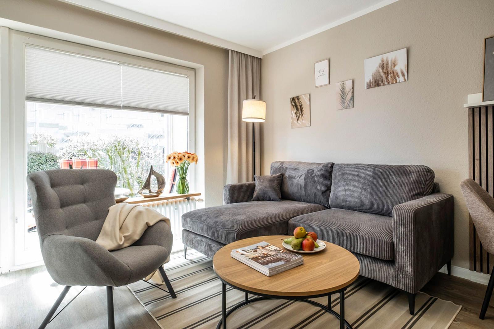 Ein Wohnzimmer mit grauem Sofa, runden Tisch und Fenster.