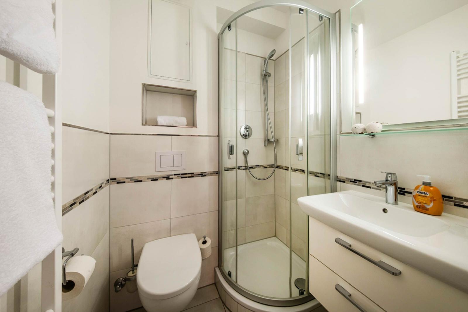 Badezimmer mit Dusche, Waschbecken und Toilette. Weiße Fliesen und Handtuchhalter.