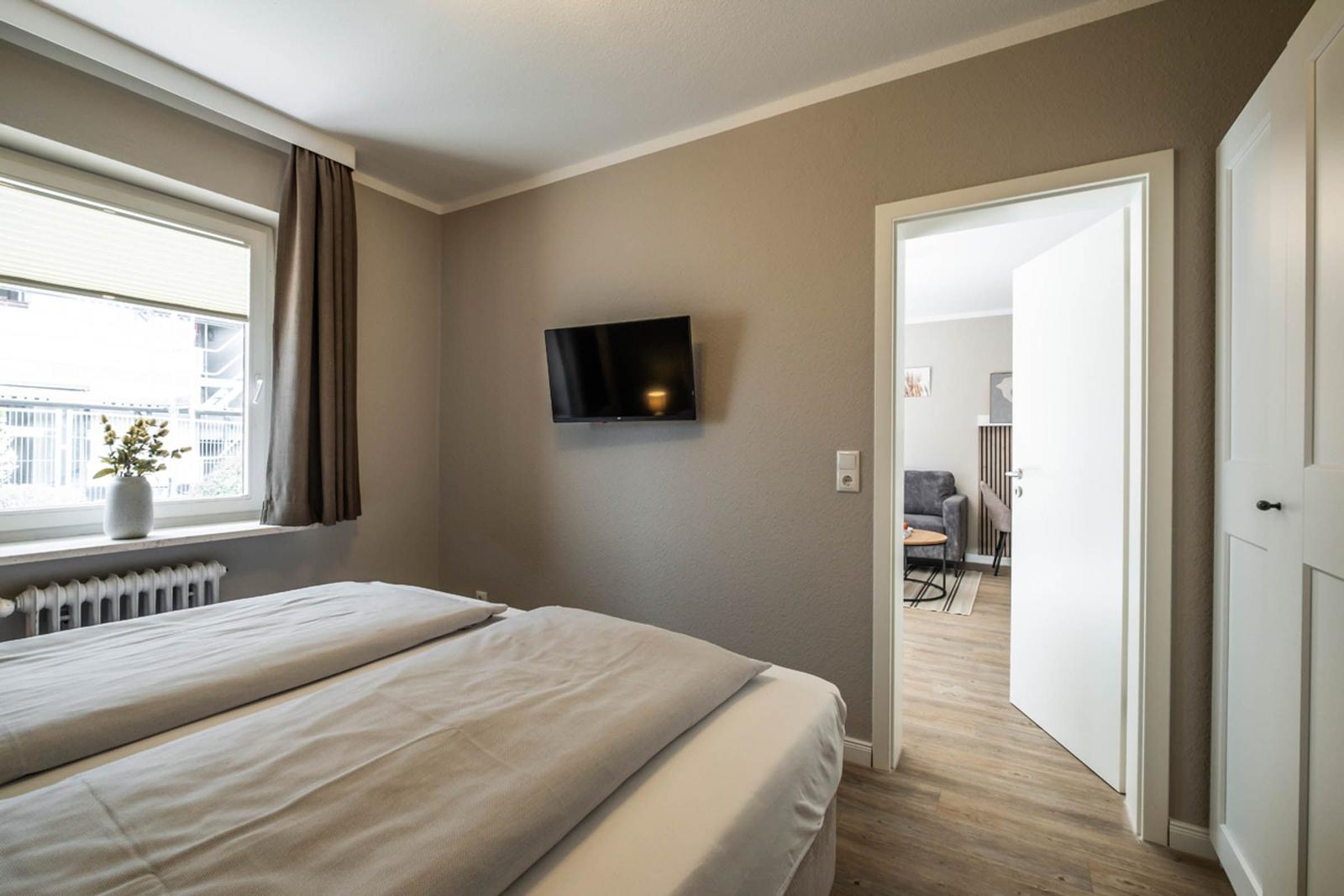 Schlafzimmer mit Bett, Wandfernseher und Fenster. Durchgang zur Wohnfläche.