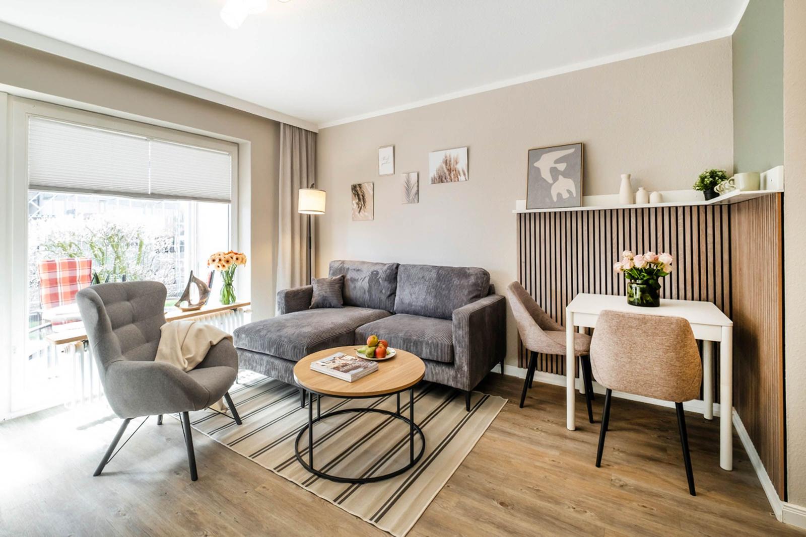 Wohnzimmer mit Sofa, Sessel, Tisch und Essbereich. Fenster mit Jalousie und Wanddekoration.