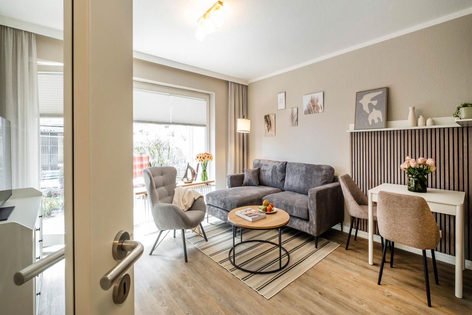 Wohnbereich mit Sofa, Sessel, Esstisch und Fenster. Holzboden und Wanddekoration.