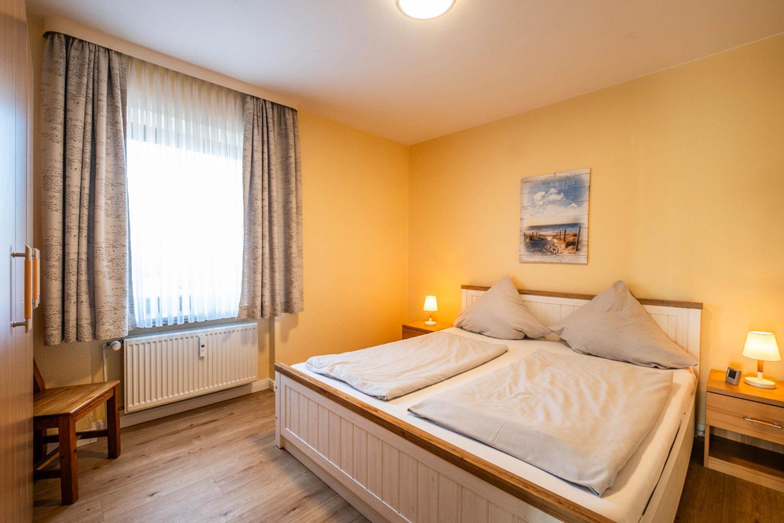 Schlafzimmer mit Doppelbett, Nachttischen und Fenster mit Vorhängen.